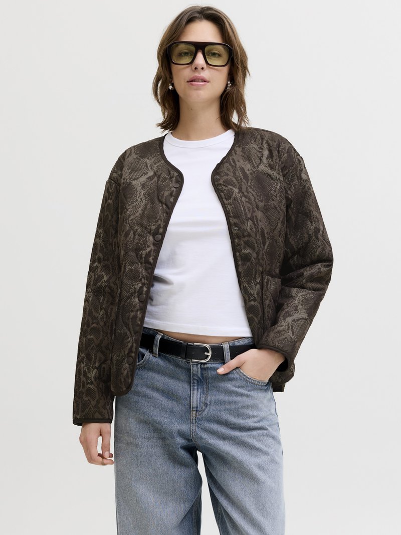 Vrouw draagt een oversized donkere jas met slangenprint over een wit shirt, lichtblauwe hoge taille spijkerbroek, zwarte riem en grote vierkante zonnebril, hand in de zak.