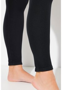 Leggings noirs côtelés avec un design ajusté, affichant une texture lisse et un léger élasticité, se terminant à la cheville avec une ourlet soigné.