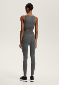 Šedý športový crop top a legíny, vyrobené z textúrovanej látky, s vysokým pásom a minimalistickým dizajnom, doplnené čiernymi teniskami.