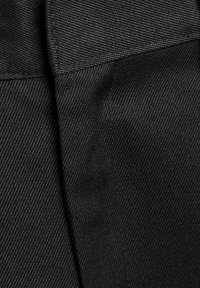 Tissu noir avec une surface texturée, présentant des coutures et un design plissé, arborant une couleur uniforme sans motifs ni éléments apparents.