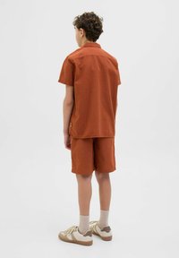 Kortärmad, texturerad skjorta i rostfärg som matchas med kortbyxor. Bärs med beige sneakers och ljusgrå strumpor. Ren, avslappnad design.