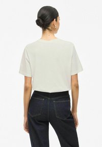 Camiseta blanca de manga corta con un corte relajado, combinada con jeans de mezclilla azul de talle alto que presentan bolsillos traseros y un corte clásico.