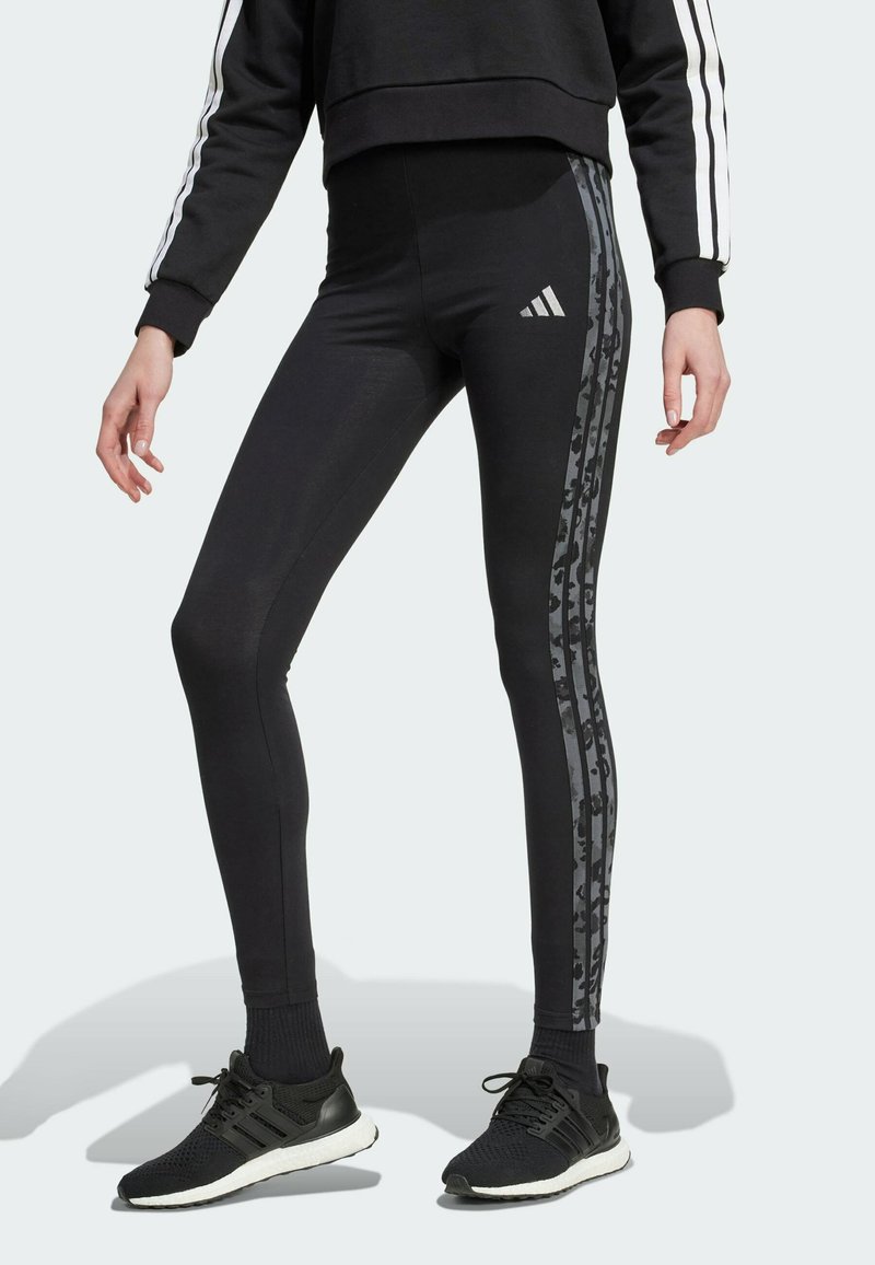 Black leggings with a high waist and a slim fit, featuring dark camo stripes down the sides and an Adidas logo in silver.