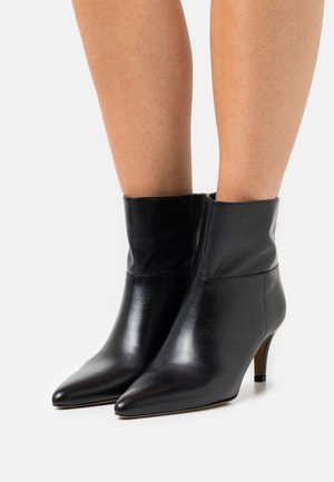Botas de cuero negras hasta el tobillo con un diseño de punta afilada, un puño doblado y un tacón delgado. Textura suave y estilo minimalista.