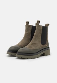 Stivaletti alla caviglia in camoscio verde oliva con pannelli laterali elastici neri, punta arrotondata, suola in gomma spessa e linguette per facilitare la calzata.