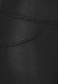 Zwarte leggings met een gestructureerde afwerking, voorzien van een kleintje achterzak en strakke stiksels. Het materiaal is rekbaar en vormgevend.