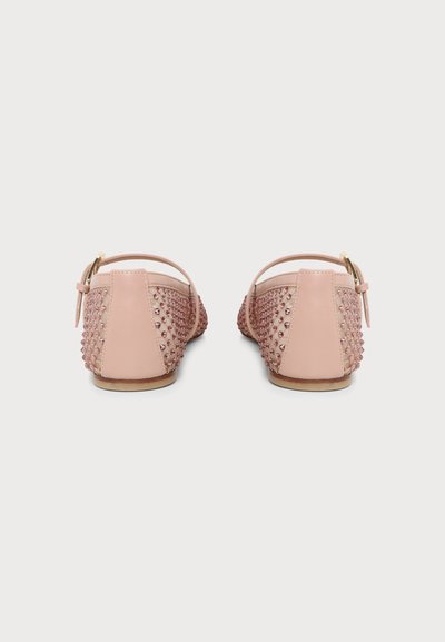 Paire de chaussures plates roses avec brides à la cheville, détails cloutés sur les côtés et talon arrière lisse, vues de dos sur fond blanc.
