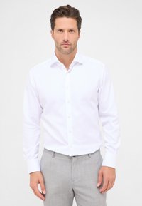 Witte langwerpige blouse van katoen met een klassieke kraag en een knoopsluiting aan de voorkant, gecombineerd met lichtgrijze broeken.