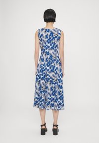 La robe midi fleurie présente des fleurs bleues sur un fond blanc, un design sans manches et une forme évasée. Des sandales à talons noires complètent le look.
