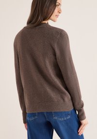 Brun tröja med en mjuk textur, rundad halsringning och ribbade muddar. Kombineras med blå denimjeans som visar en avslappnad passform.