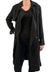 Manteau long noir en tissu léger, avec un col à revers, des boutons double boutonnage, et une coupe ample avec des manches à revers.