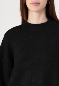 Schwarzer Strickpullover mit rundem Ausschnitt, aus einem strukturierten Stoff und mit überschnittenen Schultern für eine lockere Passform.