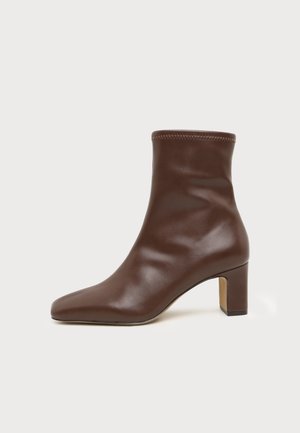 Bottine en cuir marron avec un bout arrondi et un talon bloc de hauteur moyenne sur fond blanc uni.
