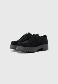 Chaussures en daim noir avec une semelle en caoutchouc épaisse et rainurée. Les caractéristiques incluent un design à lacets et des coutures contrastées le long du bord.
