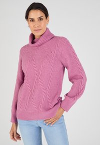 Maglione rosa lavorato a maglia con collo a barchetta, maniche lunghe e un motivo testurizzato. Presenta una vestibilità comoda e orlo a coste. Abbinato a jeans azzurri chiari.