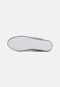 Semelle en caoutchouc blanche avec une texture antidérapante, présentant un accent bleu marine sur le bord ; design global lisse sans motifs visibles.