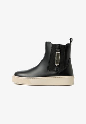 Bottine en cuir noir avec panneaux latéraux élastiques, semelle crème, accent en métal de marque et détails de couture minimalistes.