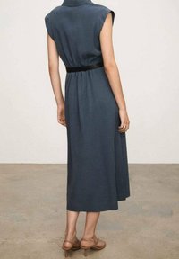 Beżowa, ciemnoniebieska sukienka bez rękawów z kołnierzykiem i czarnym paskiem w talii, sięgająca poniżej kolana, uszyta z gładkiego materiału o luźnym kroju.
