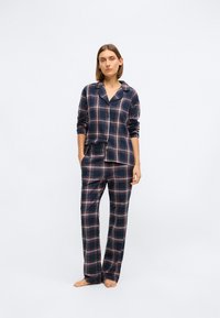 Laivastonsininen ruudullinen pyjama-asusetti, joka sisältää napitettavan paidan, jossa on kaulus ja pitkät hihat, yhdessä väljästi istuvien suoranlahkeisten housujen kanssa.