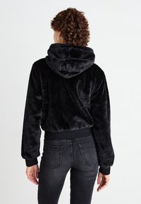 Zwarte, fluffy hoodie met een voorzak, trekkoord aan de capuchon en geribde manchetten, gecombineerd met donkere jeans die de achterzakken en textuur laten zien.