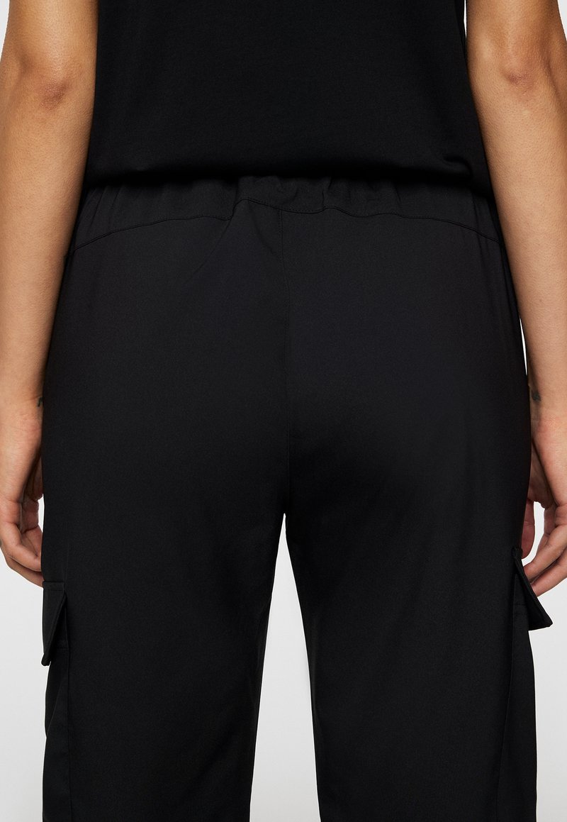 I pantaloni cargo neri presentano una texture liscia, una vita elasticizzata e tasche laterali. Il design è funzionale e minimalista.