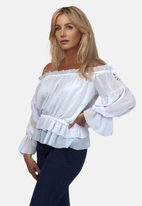 Biała bluzka na ramiączkach z przezroczystej tkaniny, z falbaniastym dołem i dzwonowymi rękawami, z wcięciem w talii.