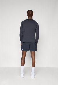 Dark long-sleeve athletic shirt paired with dark shorts, featuring a lightweight, breathable fabric. White socks and shoes complete the outfit.