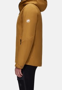 Veste imperméable jaune-brun avec capuche, arborant un logo sur la manche, des poignets réglables et des poches latérales zippées.