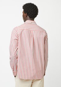 Rood-wit gestreepte shirt met een kraag, knoopsluiting aan de achterkant, lange mouwen en een plooitje aan de achterzijde voor meer bewegingsvrijheid.