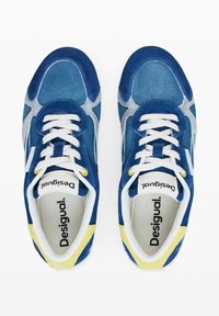 Sneakers din suede albastre cu un design gri suprapus, sireturi albe și accente galbene pe toc și gauri pentru sireturi. Branding vizibil în interior.