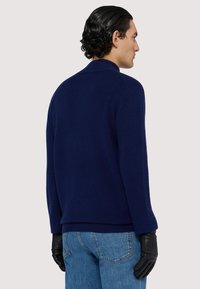 Marinblått stickat tröja med rundad krage, ribbade ärmslut och avslappnad passform; bärs med svarta läderhandskar och ljusblå jeans.