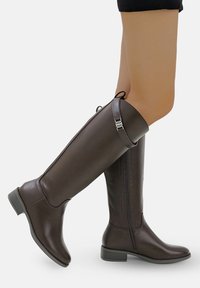 Bottes marron jusqu'aux genoux en cuir synthétique lisse, dotées d'une fermeture éclair sur le côté, de coutures contrastées et d'un petit talon carré.