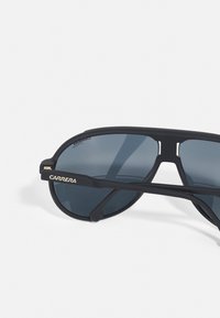 Sorte solbriller med mat finish, store mørke linser og gull "CARRERA"-logo på siden. Slank design med fremtredende rammeformer.