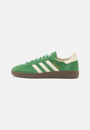 Baskets Adidas Spezial en daim vert avec des bandes blanches, talon beige, semelle texturée marron et logo doré "Spezial" sur le côté.