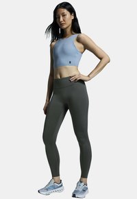 Soutien-gorge de sport bleu clair avec une finition lisse et des bretelles larges, assorti à un legging taille haute vert foncé au design élégant et aux coutures subtiles.