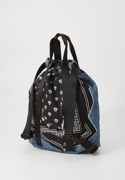 Denim en zwart stoffen trekkoord tas met bedrukte motieven, platte bodem, verstelbare schouderbanden en logo. Bevat geometrische en patroonaccenten.
