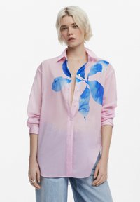 Camicetta rosa con bottoni, decorata da una stampa floreale blu nell'area del petto sinistro, maniche lunghe arrotolate, realizzata in un tessuto leggero e liscio.