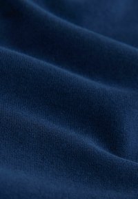 Tissu bleu foncé doux avec une texture fine en tricot visible et des plis doux créant une surface lisse et fluide.
