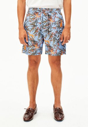 Herren leichte hellblaue Shorts mit orange-braunem Blumen- und Tiermuster, getragen mit braunen Lederloafern und einem weißen Hemd.