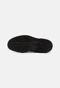 Black rubber shoe sole with a textured grip pattern and defined grooves for traction, featuring a smooth edge and reinforced heel section.