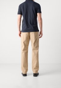 Granatowa koszulka polo z krótkim rękawem i żeberkowym kołnierzykiem, połączona z beżowymi spodniami o prostym kroju i czarnymi butami, widok z tyłu.