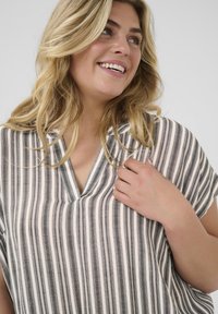 Blouse poncho rayé en tissu léger, avec un col en V, des manches courtes et des rayures grises et blanches alternées.