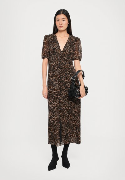 Svart og brun leopardmønstret kjole med korte pufferm, dyp V-hals og flytende stoff, kombinert med en liten svart håndveske og svarte strømpebukser.
