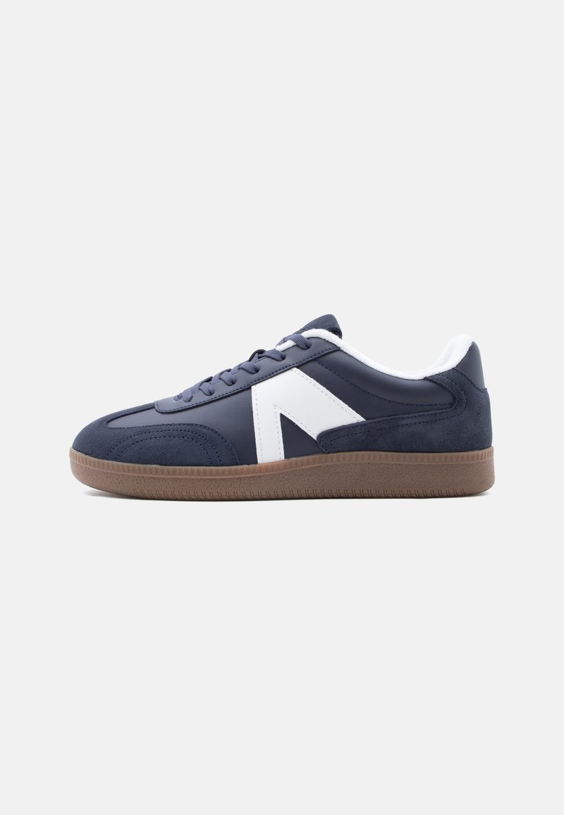 Baskets bleu marine avec un logo blanc, une semelle texturée marron, un design à lacets et un col rembourré sur fond blanc.