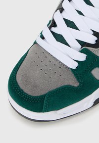 Grüne und graue Wildledersneaker mit weißen Schnürsenkeln, perforiertem Zehenbereich und strukturierten Akzenten. Schlankes Design und kontrastierende Materialien hervorgehoben.