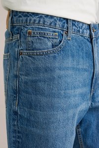 Plave traperice s malo izblijedjelim završetkom, s klasičnim džepovima, bakrenim zakovicama i kontrasnim šavovima duž šavova.