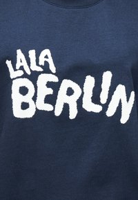 Μπλε μπλε φούτερ με άσπρο, αφράτο κείμενο που γράφει "LALA BERLIN", με στρογγυλή λαιμόκοψη και μαλακή υφή.