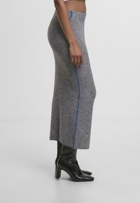 Grauer gerippter Strickrock mit blauem Seitestreifen, der ein langes, eng anliegendes Design und einen hohen Taillenbund hat, kombiniert mit schwarzen Stiefeletten mit Absatz.