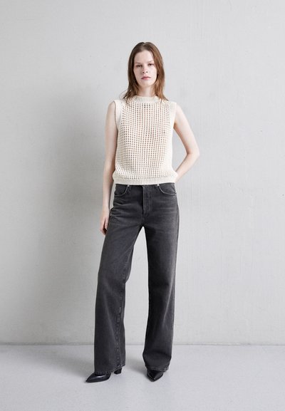 Cream knitted sleeveless top with textured pattern, paired with high-waisted, loose-fitting dark gray jeans and pointed black heels.