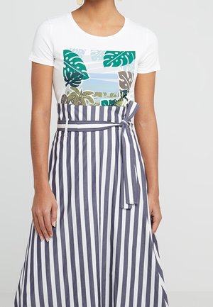 Weißes T-Shirt mit grün-blauem tropischen Druck, kombiniert mit einem marineblauen und weißen gestreiften Rock mit Taillenknoten.